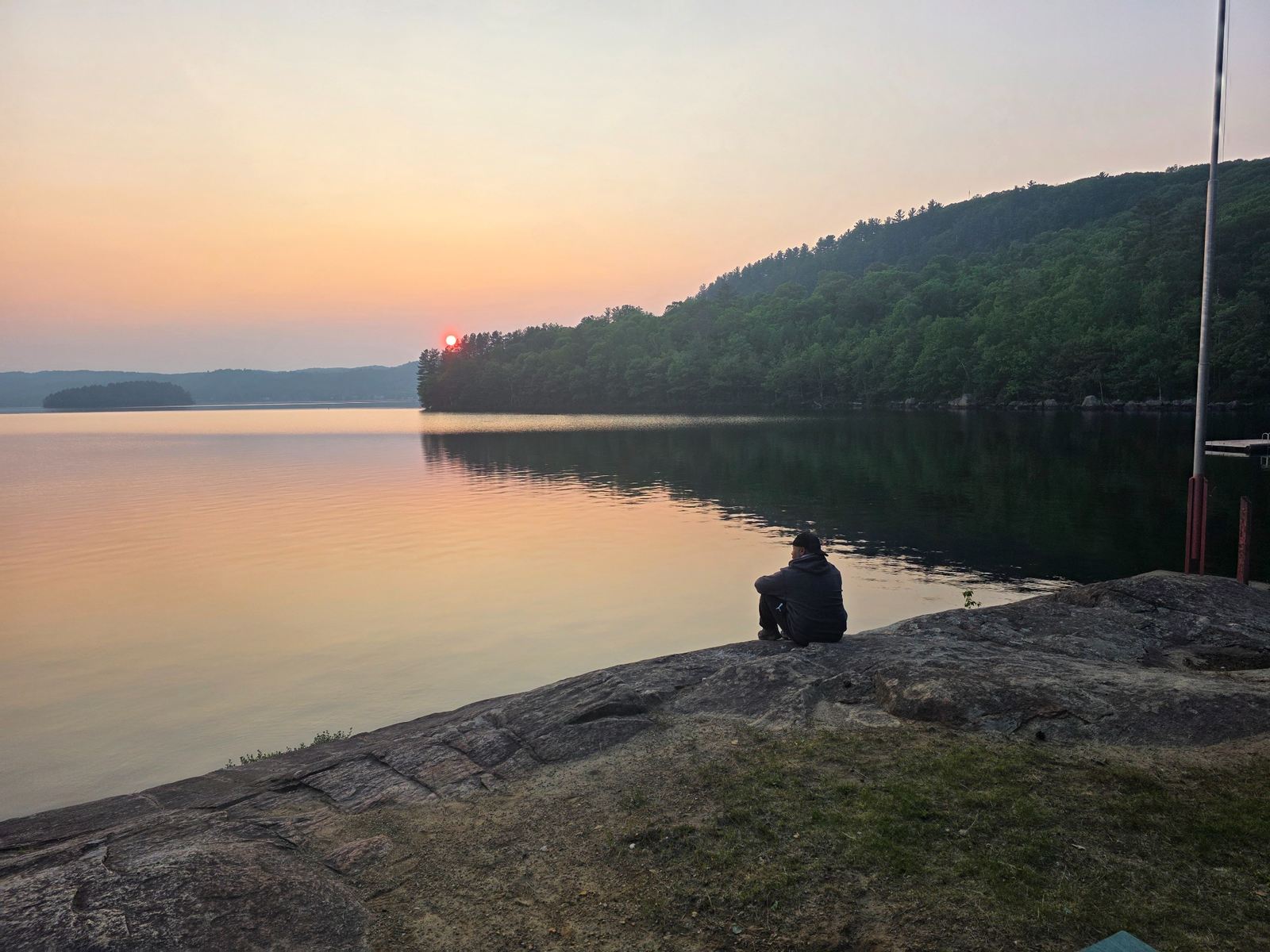 A person sitting by a calm lake at sunset
