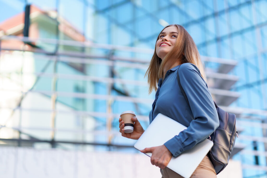 portrait smiling woman holding laptop and coffee outdoors